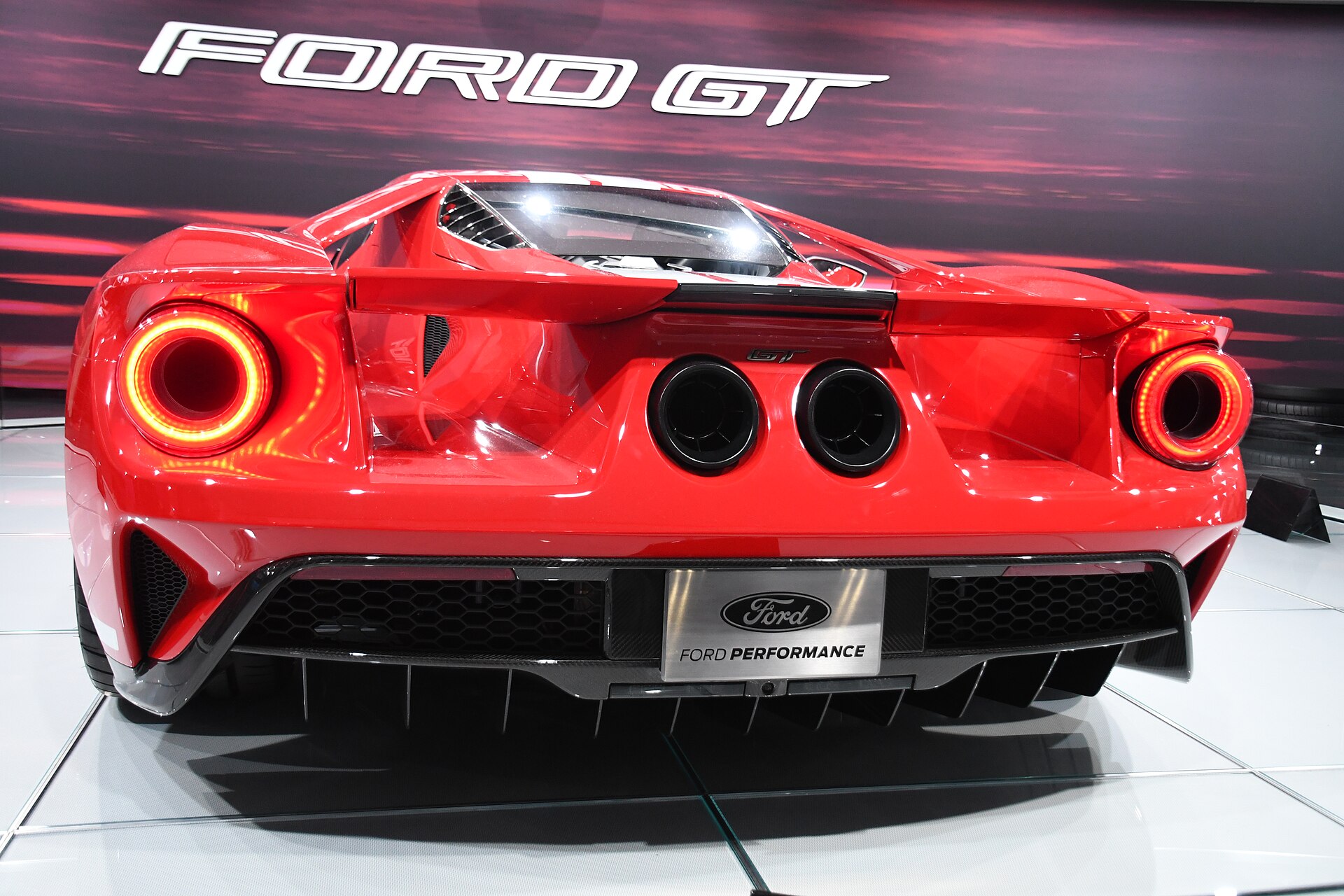 Ford GT seen dead-on from the rear: round tail lamps lit, flying buttresses framing the exposed wing