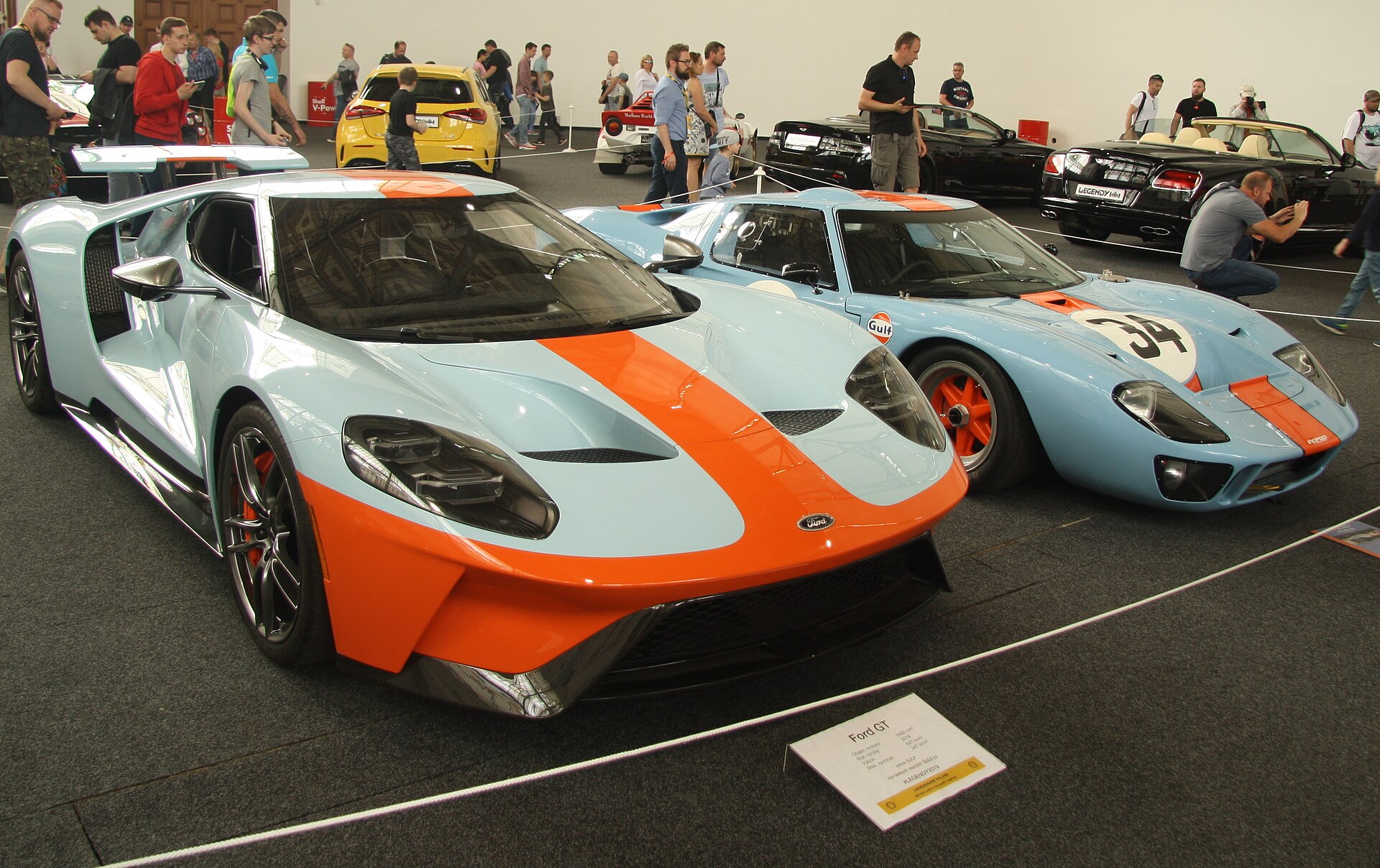 A Gulf-liveried second-generation Ford GT parked beside an original 1968 GT40 — powder blue, marigold stripe, fifty years apart