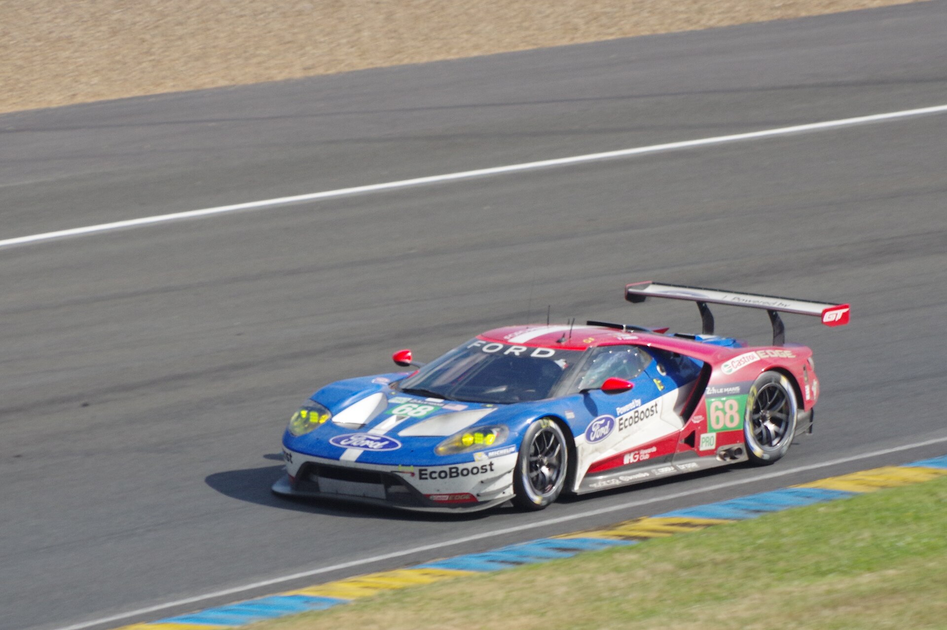 The number 68 Ford GT race car at speed on the Le Mans circuit, red-white-blue works livery
